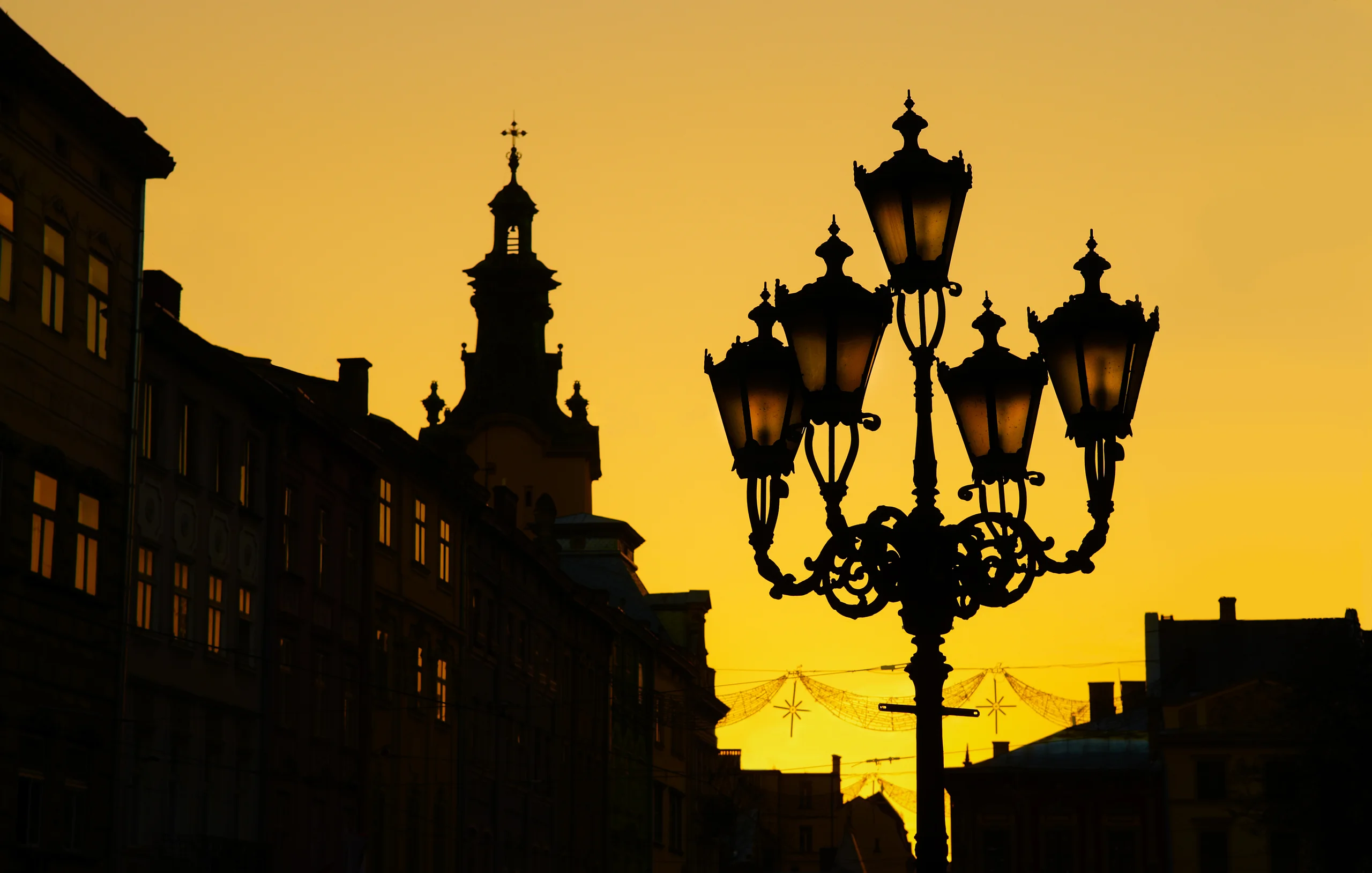Ornate street lanterns and old buildings silhouetted against a golden yellow sky.