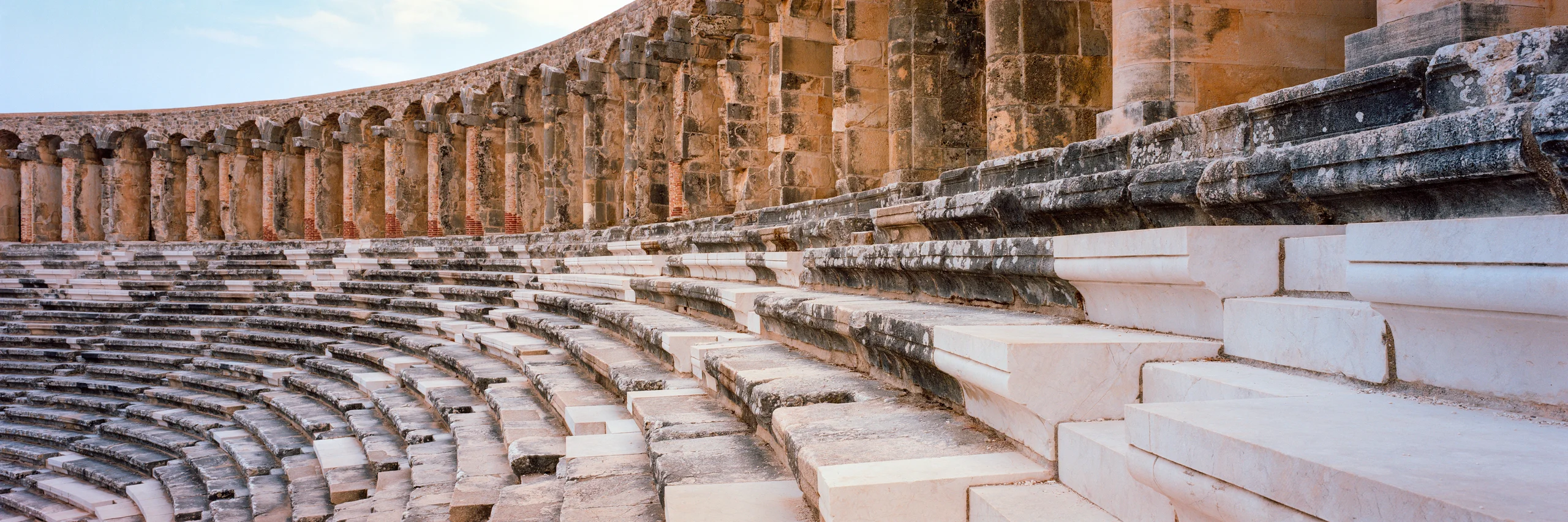 Curving rows of weathered stone theatre seats beneath a wall of arches.
