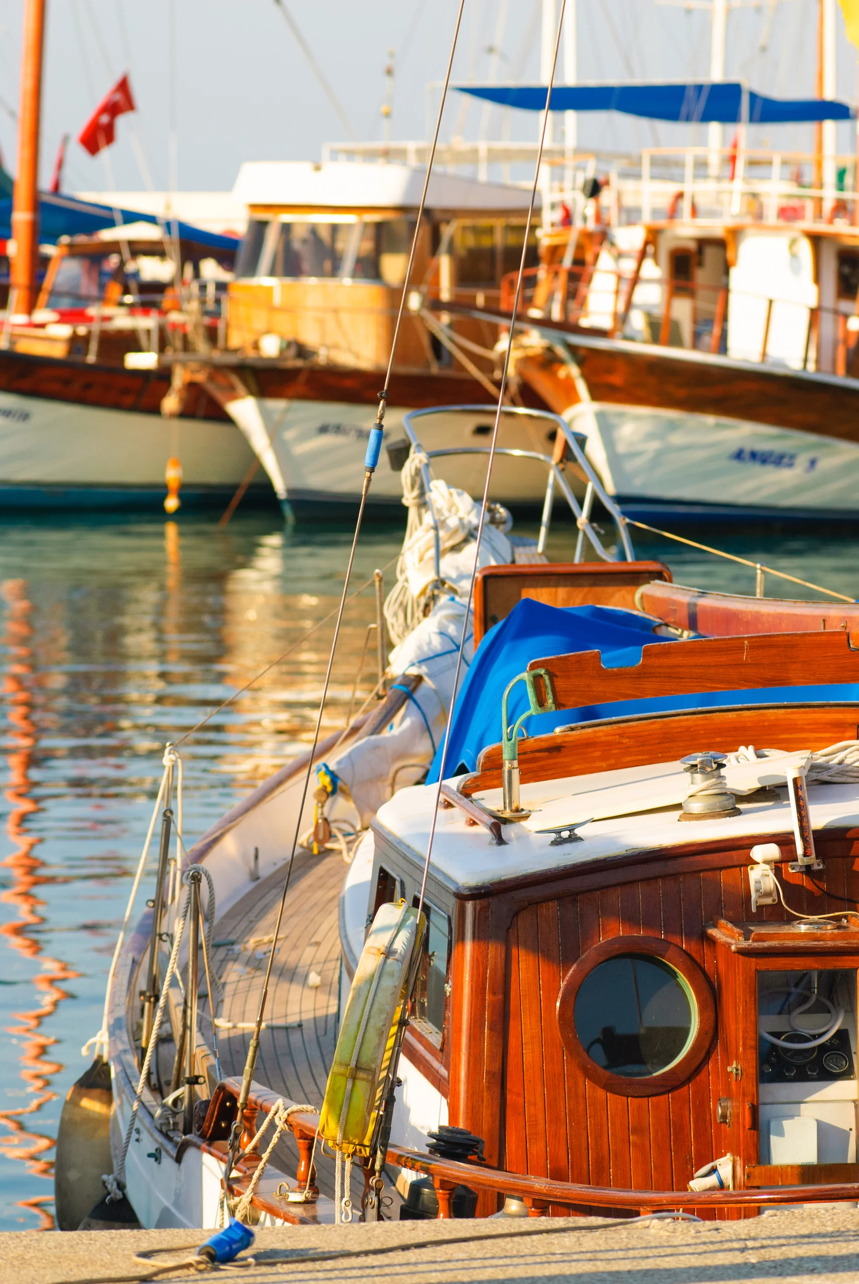 Moored wooden boats with blue canvas, white hulls, ropes and warm reflections in harbour water.