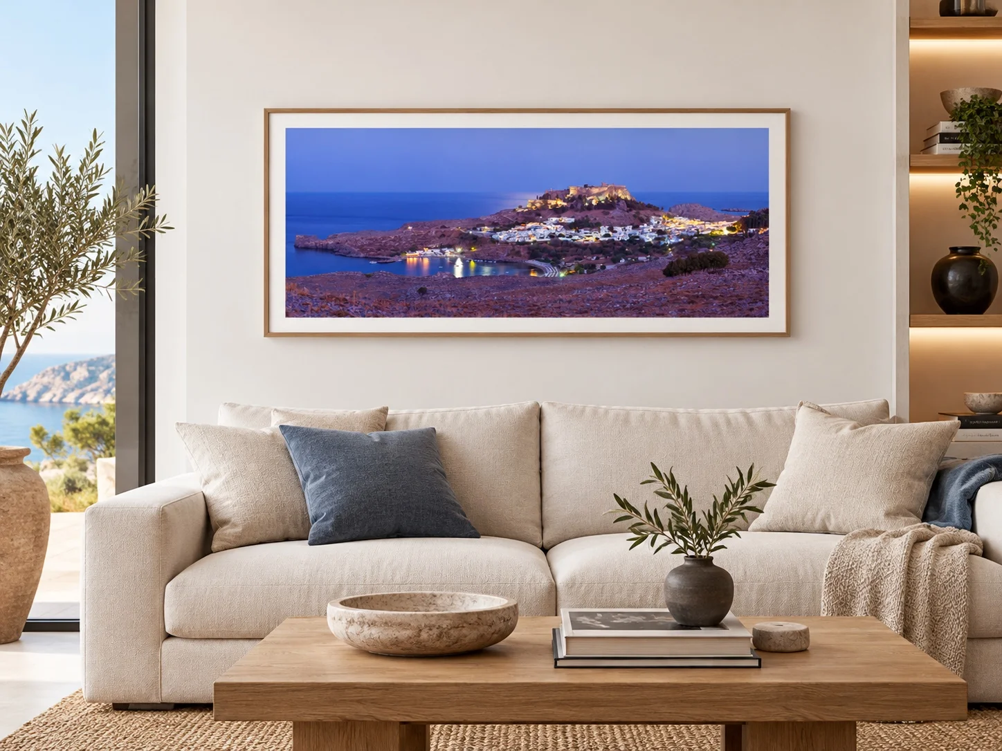 Illustrative mockup: The Village Lights in a wooden frame with a light mat above a cream sofa in a coastal living room.