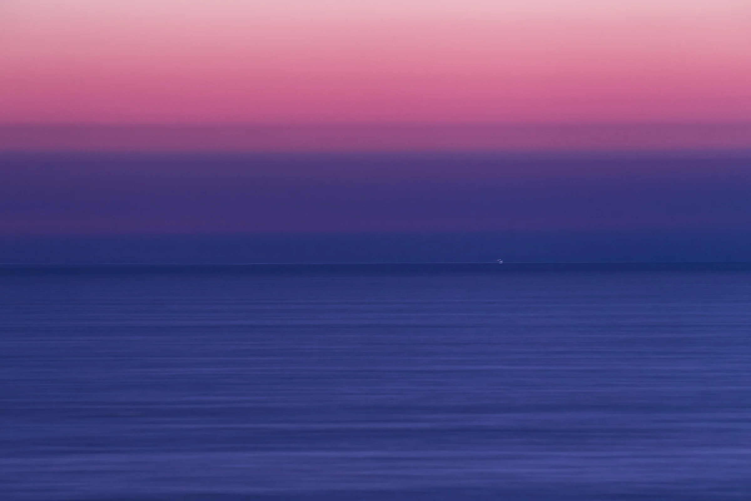 Calm blue sea beneath a pink and violet sky, with a tiny vessel near the horizon.