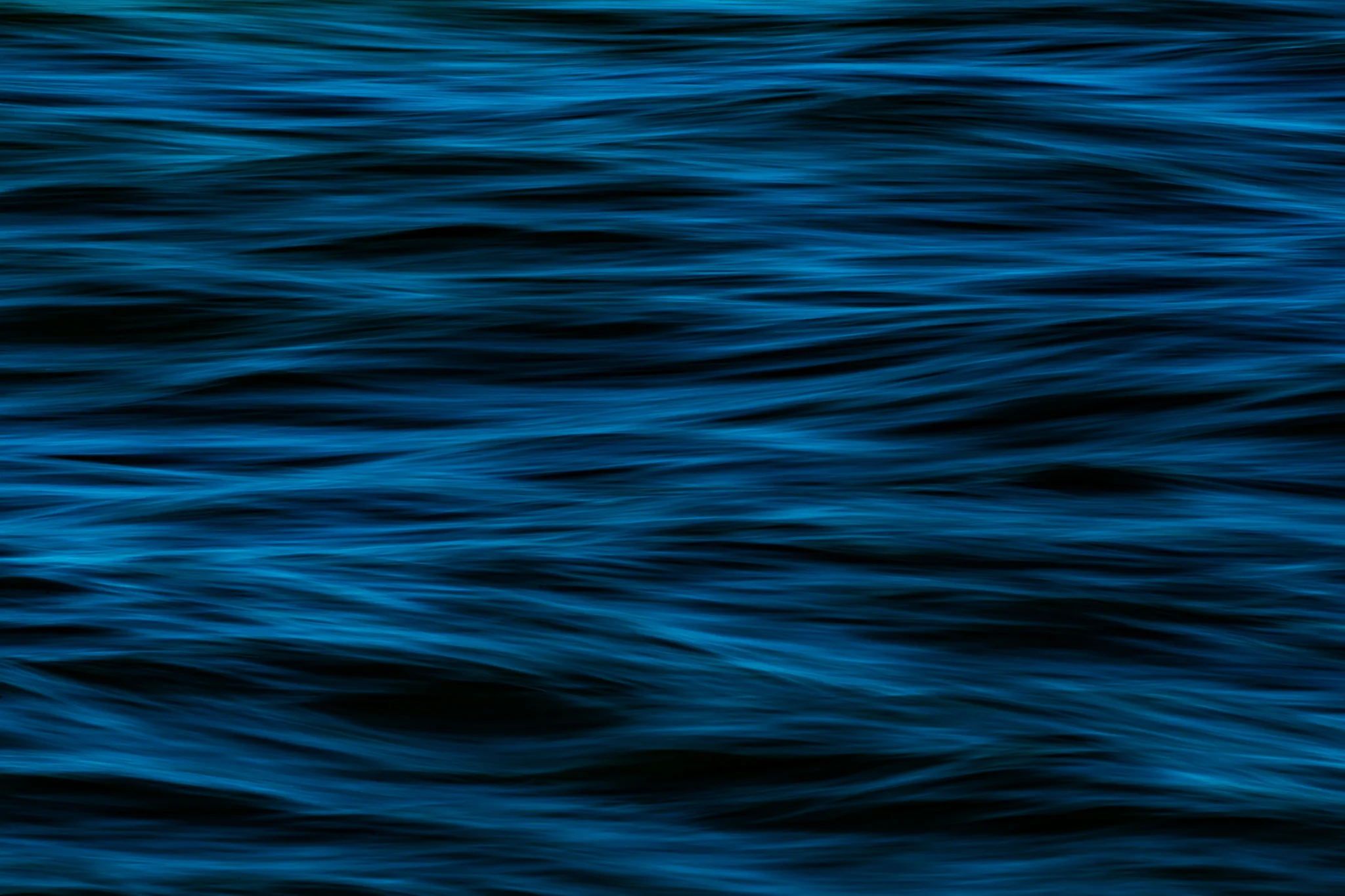 Elongated blue and teal ripples sweeping across a dark water surface.