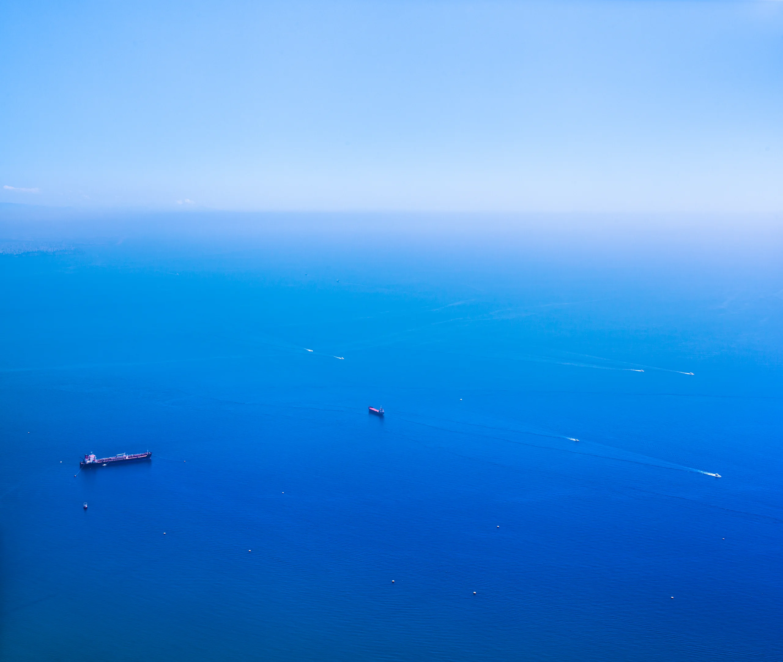 Tiny ships and white boat wakes scattered across blue water fading into a hazy horizon.